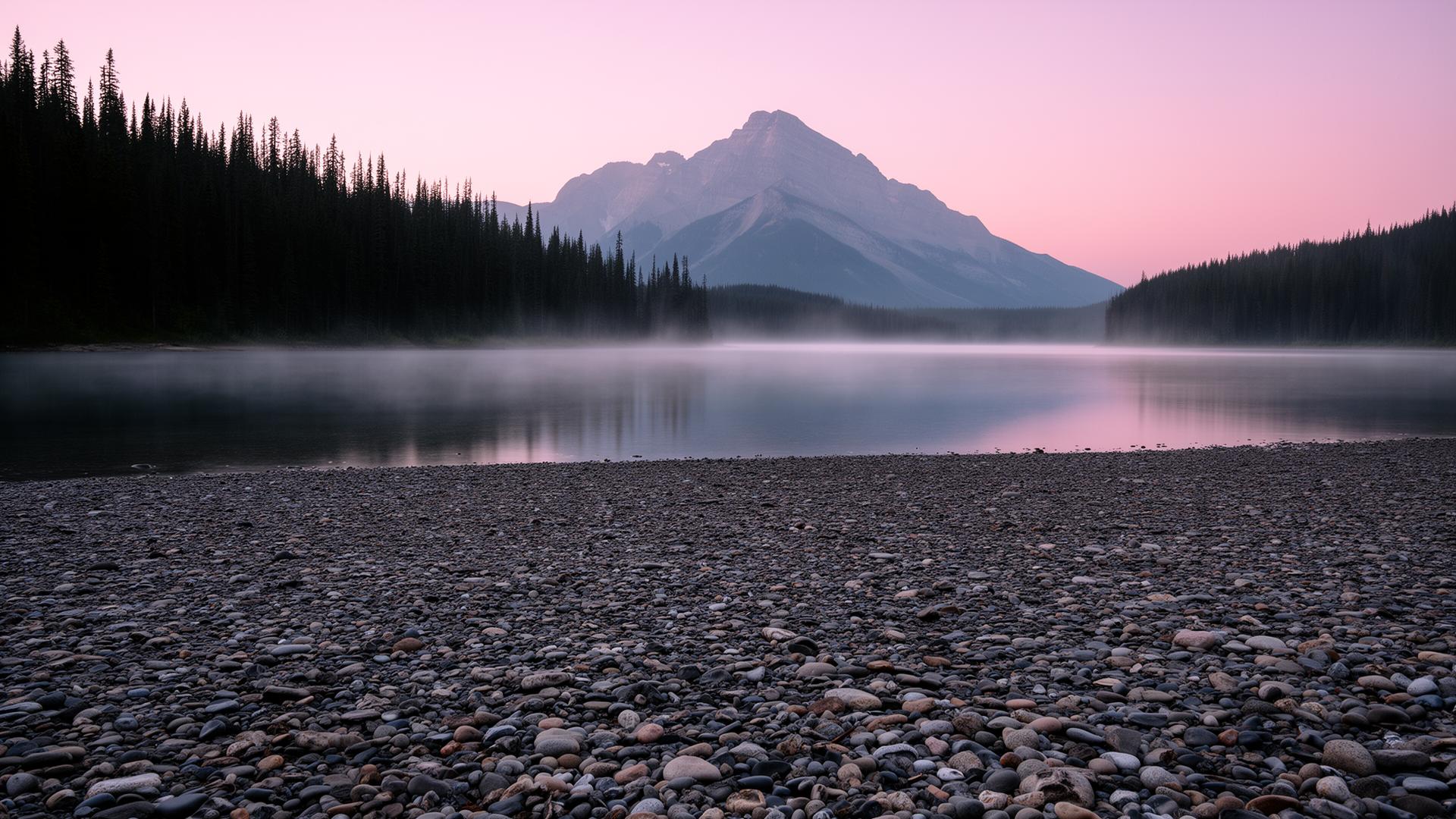 Empty pebble shoreline at a glacial alpine lake in the Canadian Rockies at dawn with mist on the water