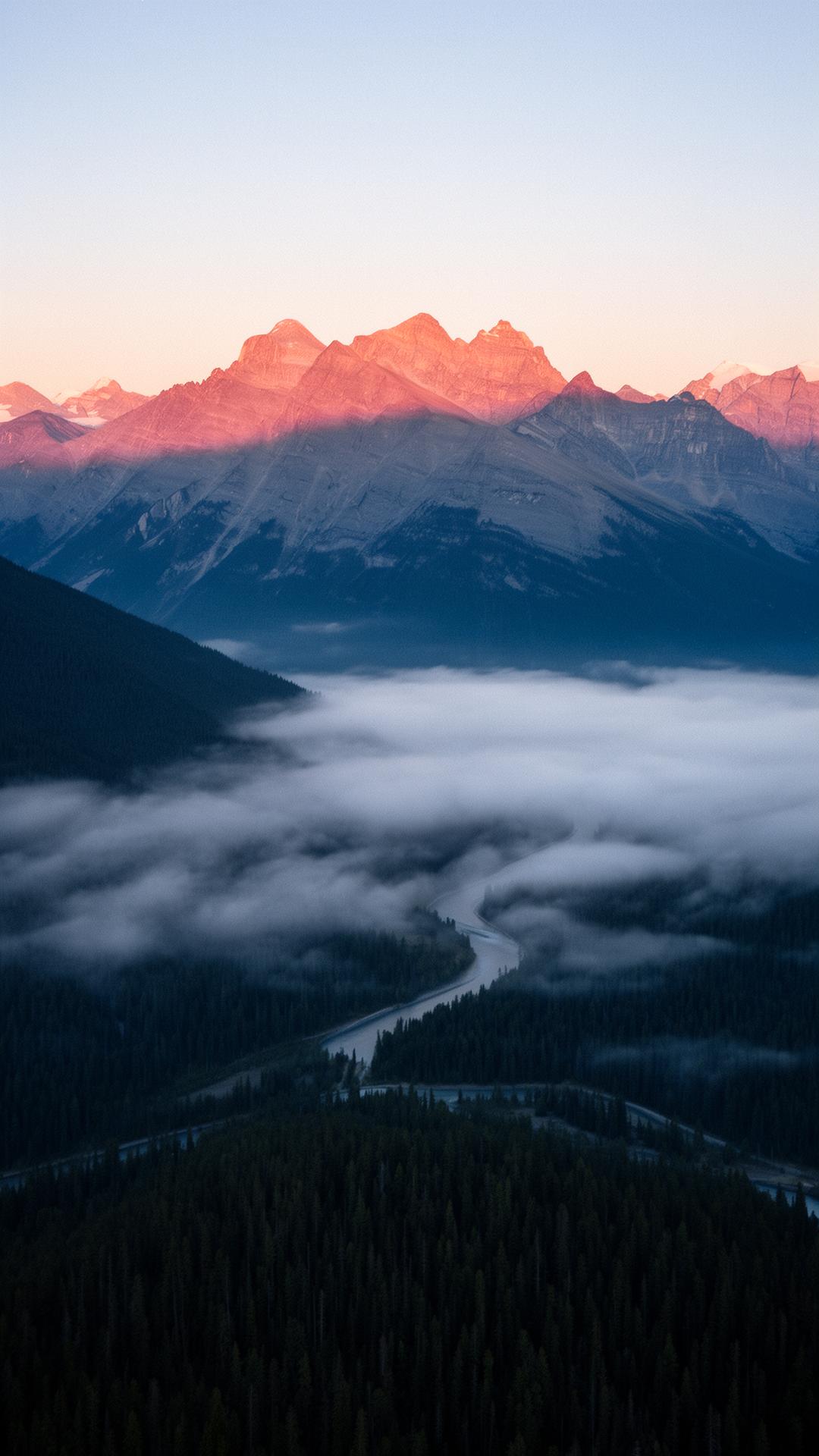 Pre-dawn alpenglow on the Canadian Rockies, mist pooling in the valley below at 4:55 AM