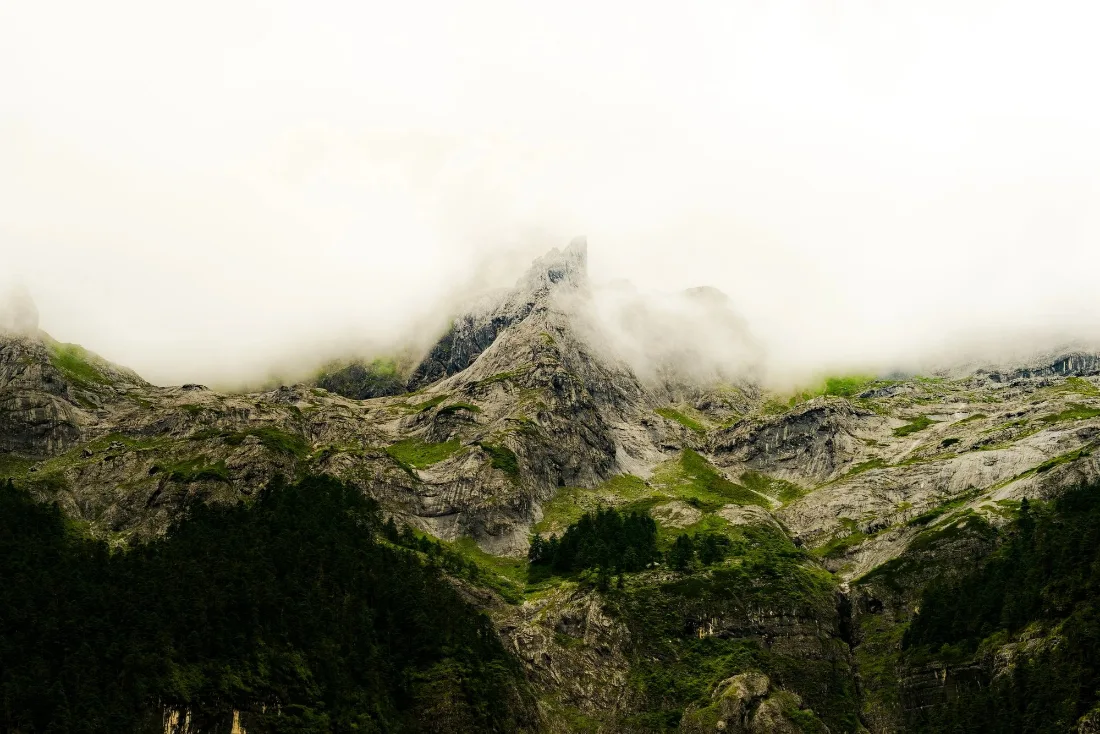 Serrated grey rock peaks and green gullies with a bank of low white cloud sitting flat across the summits.